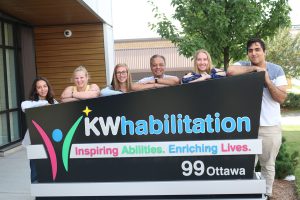 Summer Jobs students smiling outside with the KW Habilitation sign.