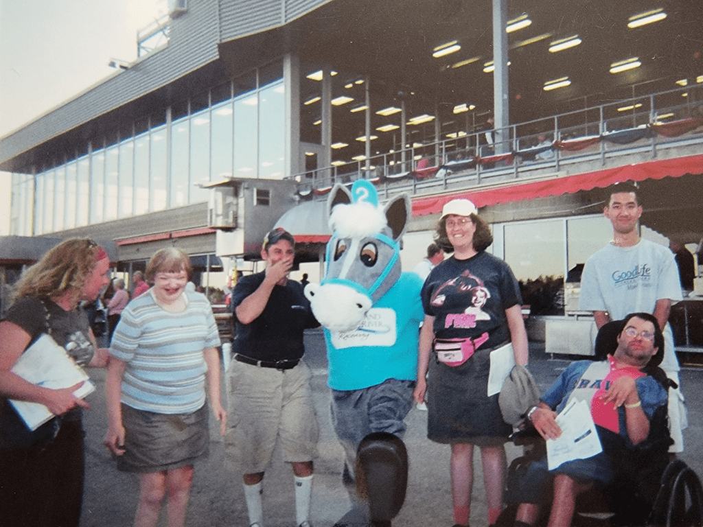 Old photo of staff and people we work for out at an event posing with a horse mascot!