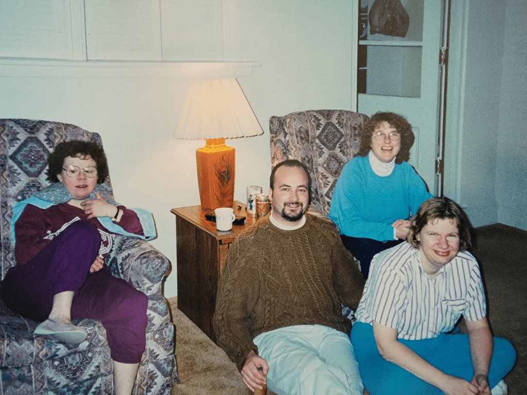 Old photo of staff and people we work for sitting in a living room with vintage patterned chairs.