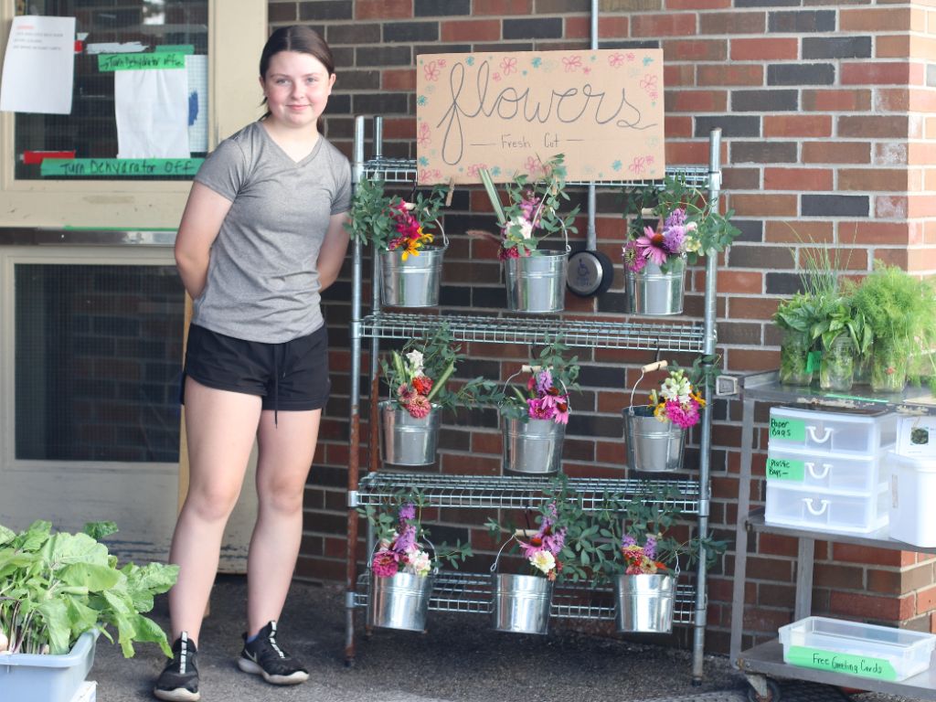 KW Habilitation's Our Farm student volunteer smiling beside cart of fresh cut flowers grown at Our Farm.