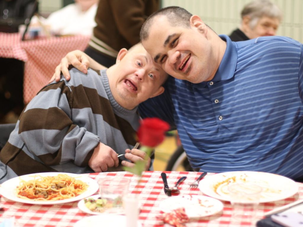 Two adults with disabilities smiling at the dinner table at KW Habilitation's annual spaghetti dinner.