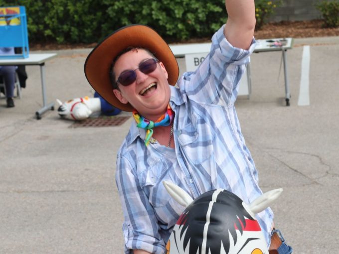 Staff member at KW Habilitation smiling and cheering while riding an inflatable horse and wearing a cowboy hat at our 2023 Staff Appreciation event.