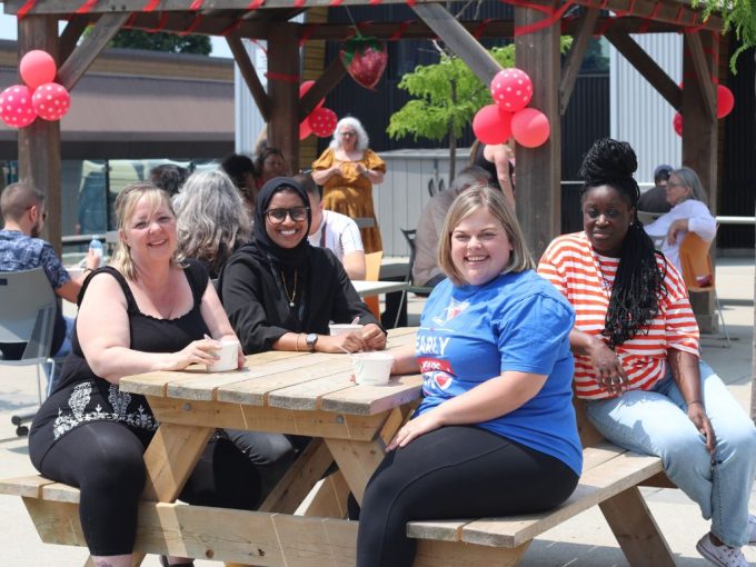 Four Resource Consultants from our Early Learning department sitting outside at a picnic table smiling while enjoying dessert during our Strawberry Social.