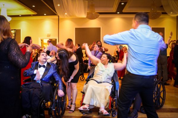 Two people with disabilities in wheelchairs dancing in a crowd of people at the KW Habilitation 50th Anniversary Gala.
