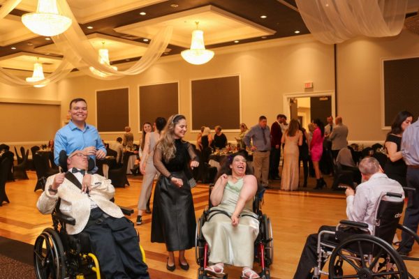 Three people with disabilities in wheelchairs dancing on the dance floor with two supporting staff at KW Habilitation during KW Habilitation's 50th Anniversary Gala event.