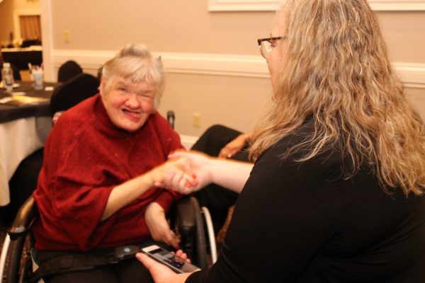 Adult with disability in wheel chair shaking hands with staff member at KW Habilitation.