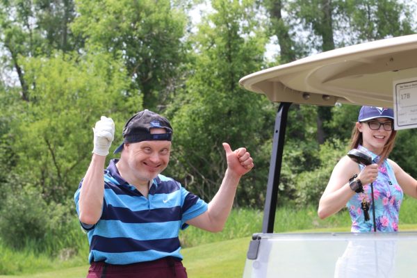 Adult with a disability smiling with supporting staff from KW Habilitation at the annual golf tournament.