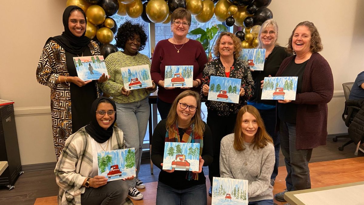 9 people from Early Learning smiling while holding their Christmas paintings.